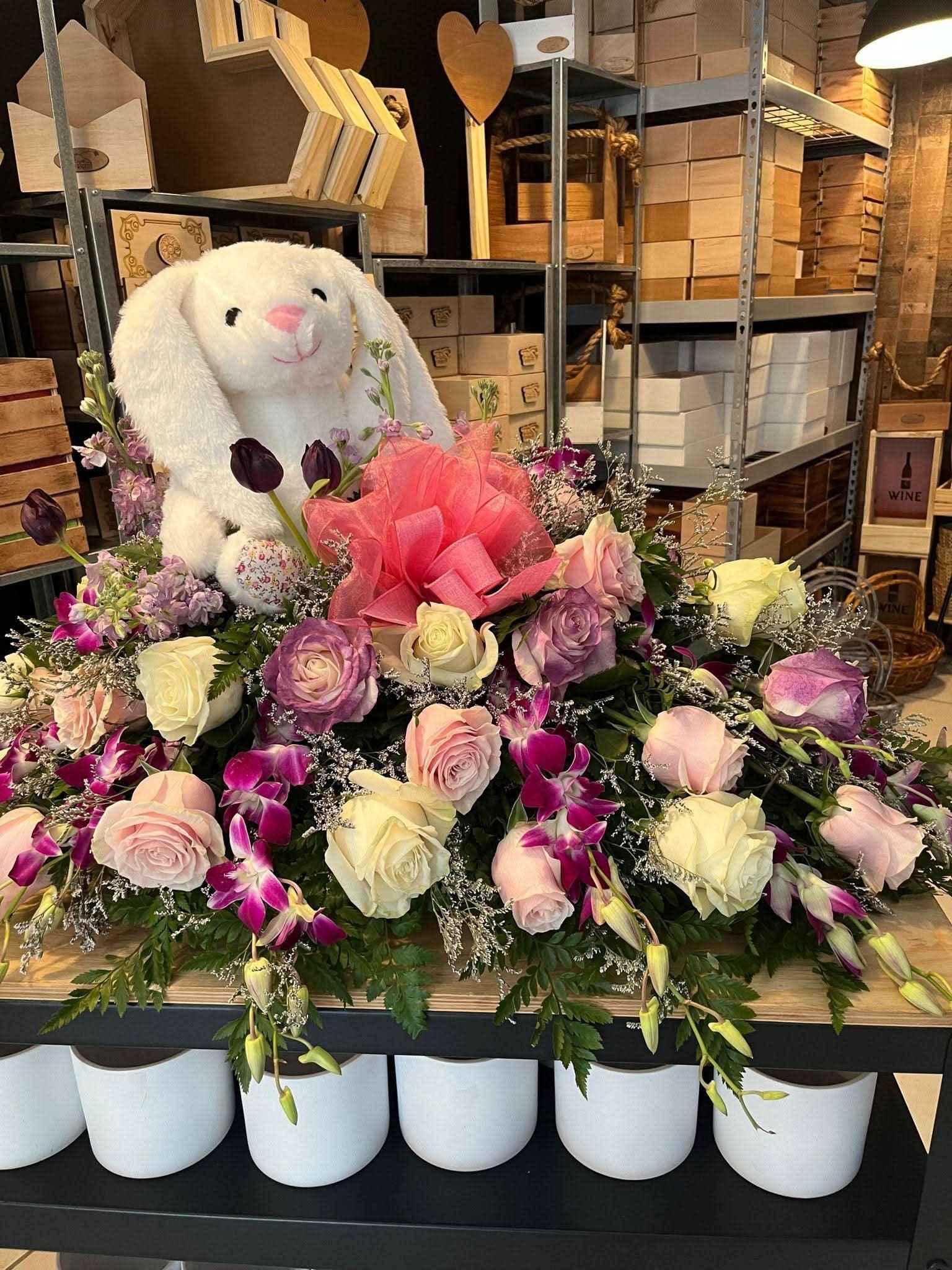 Arreglo floral para bebé con rosas, orquídeas y peluche blanco en ambiente de tienda.