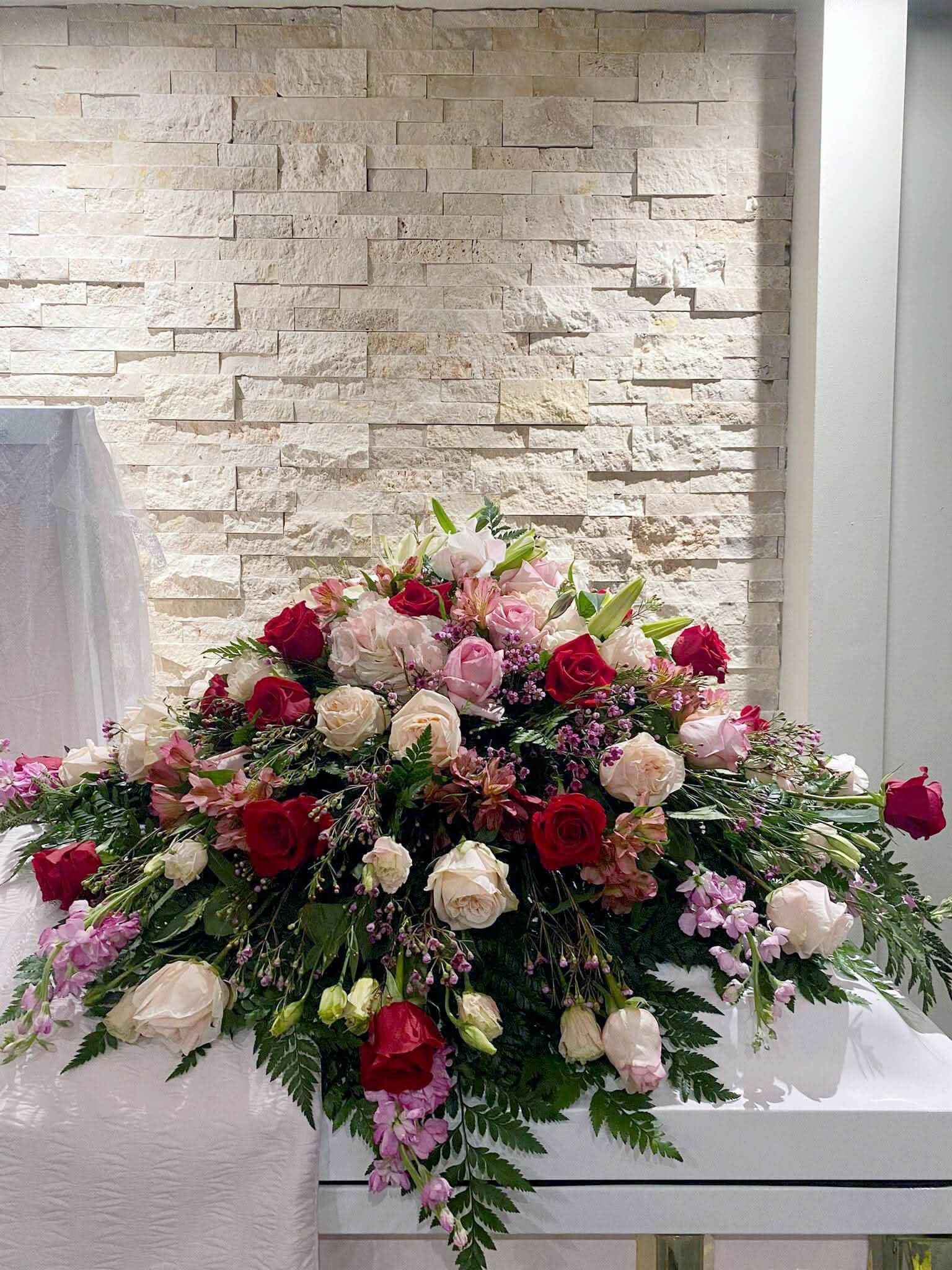 Arreglo floral sobre ataúd con rosas rojas, blancas y flores frescas para servicio funerario