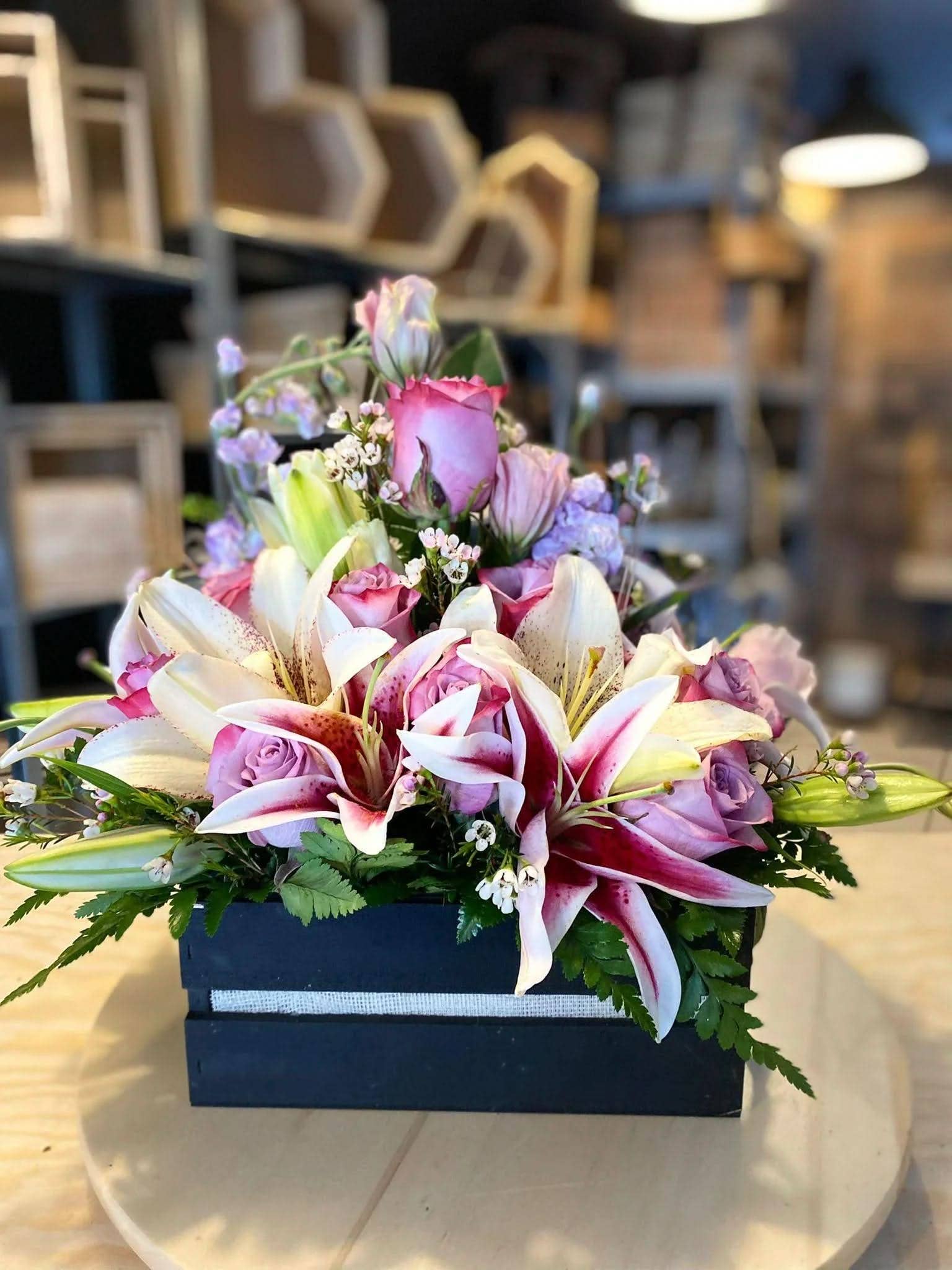 Arreglo floral con lirios y rosas rosas en caja negra sobre mesa de madera