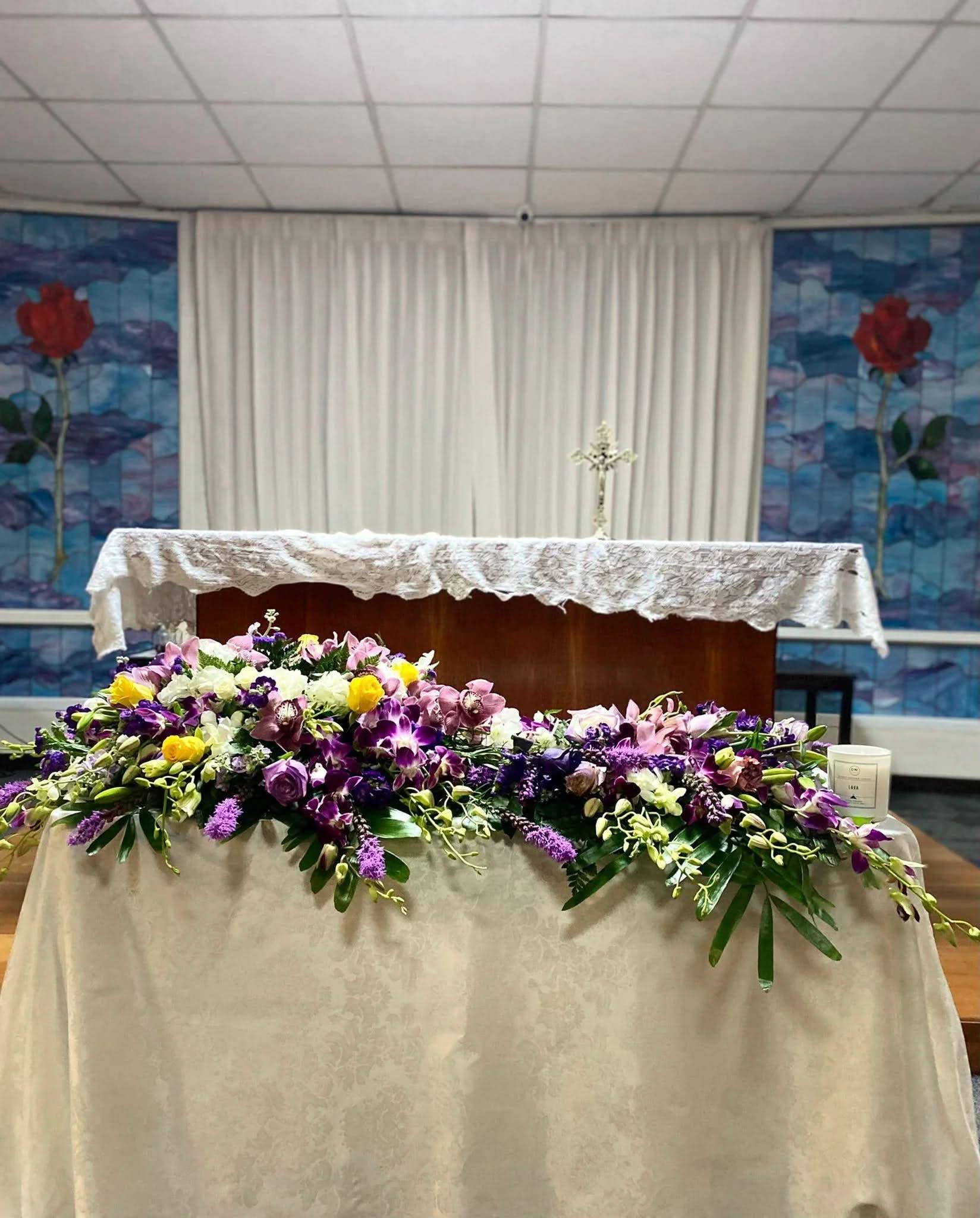 Porta cenizas decorado con flores frescas moradas, amarillas y blancas en altar funerario